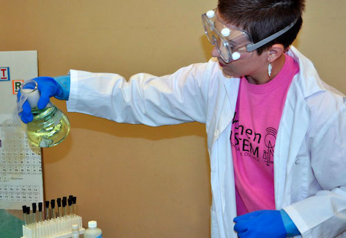 student in a lab coat pouring smoking liquid from a beaker